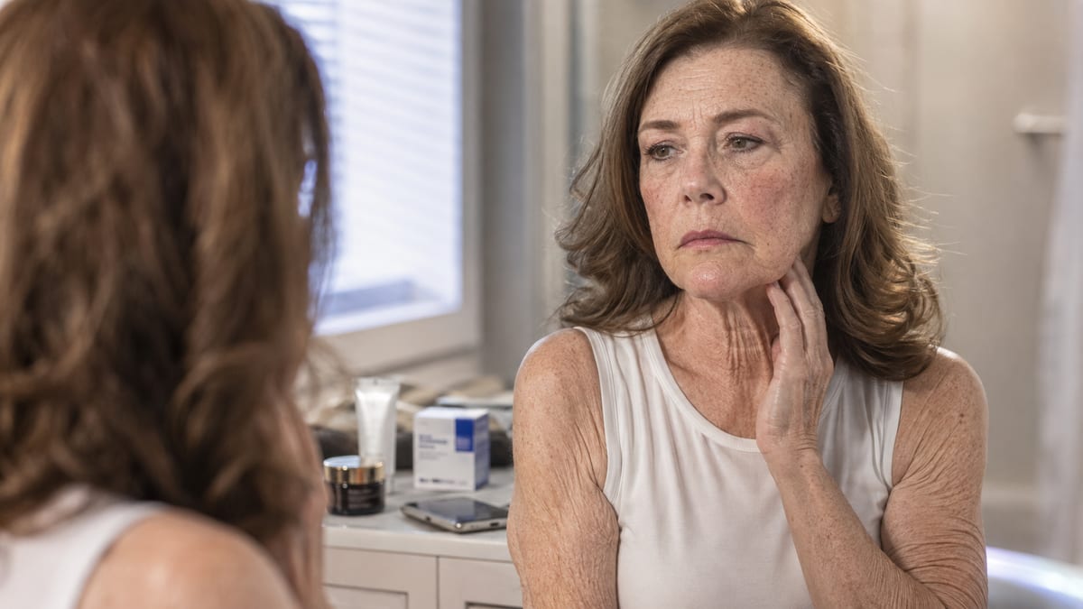 Woman in her fifties examining her sagging neck skin in a bathroom mirror